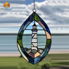 a stained glass window with a lighthouse in the center hanging from a chain on a beach