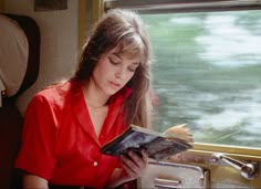 a woman reading a book while sitting on a train next to a window and looking out the window