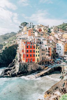 the colorful buildings are on top of the hill by the water's edge, with waves crashing in front of them