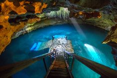 the stairs lead down to an underground pool with blue water and light coming from above