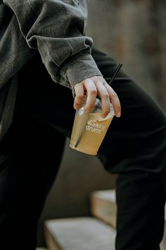 a person holding a drink in their hand while sitting on some steps with one hand