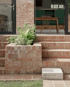 a brick patio with steps leading to the back door and dining table in the background