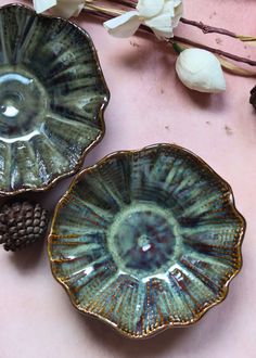 two dishes sitting on top of a table next to flowers and pineconi cones