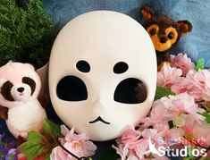 two stuffed animals and a white mask on a blue background with pink flowers in the foreground