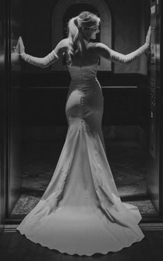 a woman in a long dress is standing by a glass door with her arms stretched out