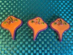 three decorated cookies sitting on top of a blue tablecloth covered surface with green and purple designs