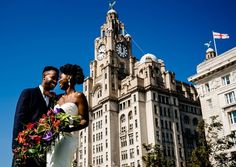 a bride and groom standing in front of a tall building with a clock on it