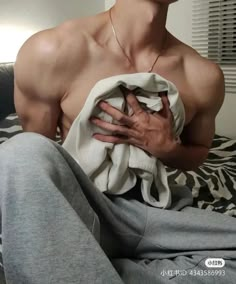 a shirtless man sitting on top of a bed holding his hands in his chest