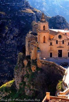 an old church perched on the side of a cliff with mountains in the back ground