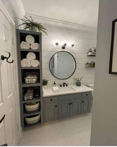 a bathroom with gray cabinets and white towels on the shelves, mirror above the sink