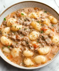 a white bowl filled with meat and dumplings on top of a marble countertop