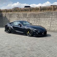 a black sports car parked in front of a stone wall