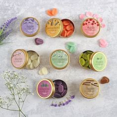 six tins of different flavored candies on a white surface next to flowers