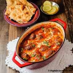 a red pot filled with food next to some pita bread and lemon wedges