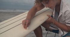 a woman kneeling down next to a surfboard