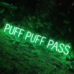 a green neon sign that says puff puff pass on it's side in the grass