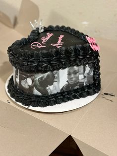 a black cake with pink and white pictures on it sitting on top of a cardboard box