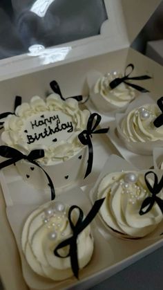 some cupcakes with white frosting and black ribbon on them in a box