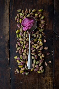 a spoon filled with nuts on top of a wooden table next to a pink flower