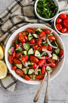 a white bowl filled with cucumber, tomato and onion salad next to lemon wedges