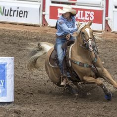 a woman riding on the back of a brown horse in a dirt field next to a white sign