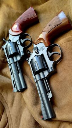 two revolvers sitting on top of a bed next to each other with the grips down