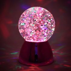 a pink snow globe sitting on top of a red stand with colored lights around it