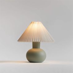 a green lamp with a white shade on it's base and a light bulb in the middle