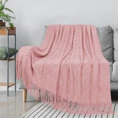 a living room with a gray couch and pink blanket on top of the sofa, next to a potted plant