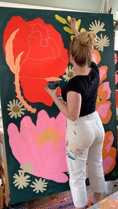 a woman is painting flowers on a large piece of art