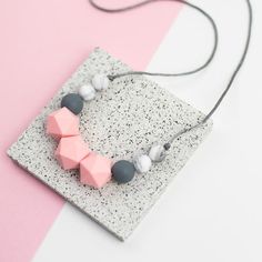 a necklace with pink, grey and white beads on it sitting on top of a tile block