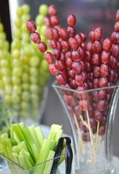 grapes and celery in a glass vase on a table with other fruits and vegetables