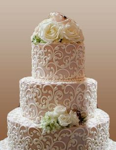 a three tiered wedding cake with white flowers on the top and bottom layer is decorated in filigree lace