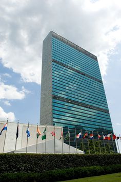 an office building with many flags in front of it and a blue sky behind it