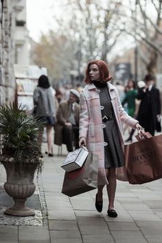 a woman with red hair carrying shopping bags and walking down the street in front of people