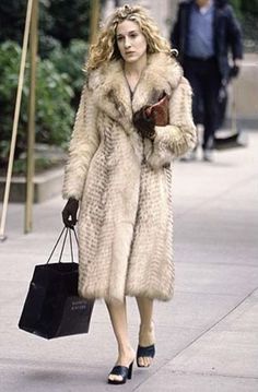 a woman is walking down the street with a shopping bag in her hand and wearing a fur coat