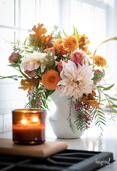 a white vase filled with lots of flowers next to a lit candle