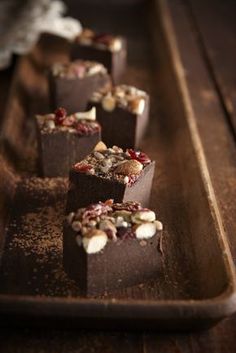 several pieces of chocolate with nuts and cranberries on top sitting on a tray