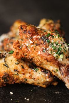 two pieces of chicken with parsley on top sitting on a black surface next to some seasoning