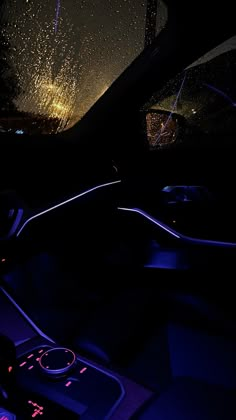 the interior of a car at night with bright lights and rain falling on the windshield