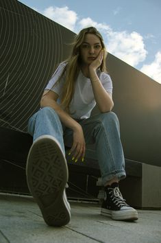 a young woman sitting on top of a bench next to a building with a blue sky in the background