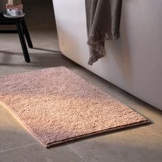 a bathroom rug that is on the floor next to a bathtub with a towel hanging over it