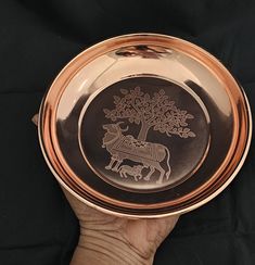 a hand holding a copper plate with an image of a horse and tree on it