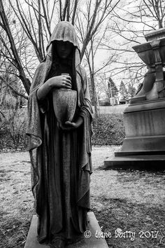 black and white photograph of a statue in a park with trees behind it, holding a baby jesus