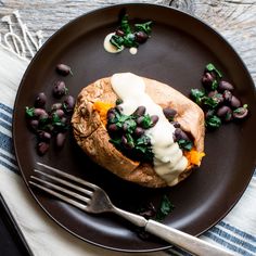 a baked potato with black beans and spinach on a plate next to a fork