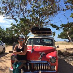 a woman standing in front of an old red truck with a surfboard on top