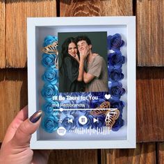 a hand holding up a photo frame with blue paper flowers