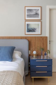 a bed sitting next to a night stand with two pictures on the wall above it