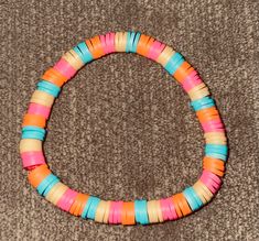 a bracelet made out of multicolored paper beads on a brown carpeting surface