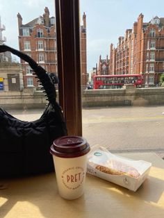 a cup of coffee sitting on top of a table next to a bag and some food